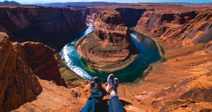 A couple dangle their feet on the edge of the Grand Canyon, the Colorado River visible below