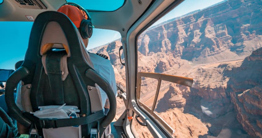 A pilot drives a helicopter over the Grand Canyon on a sunny day