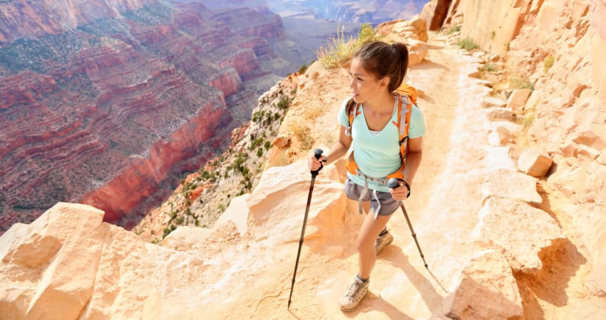 A woman hikes into the Grand Canyon with a backpack and hiking poles