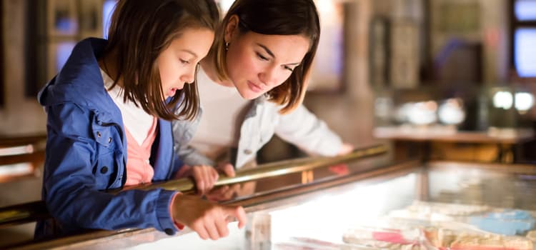 a woman and a child look closely at a museum display in a glass box