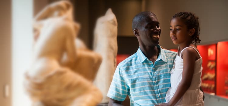 a man holds his child in front of a museum sculpture