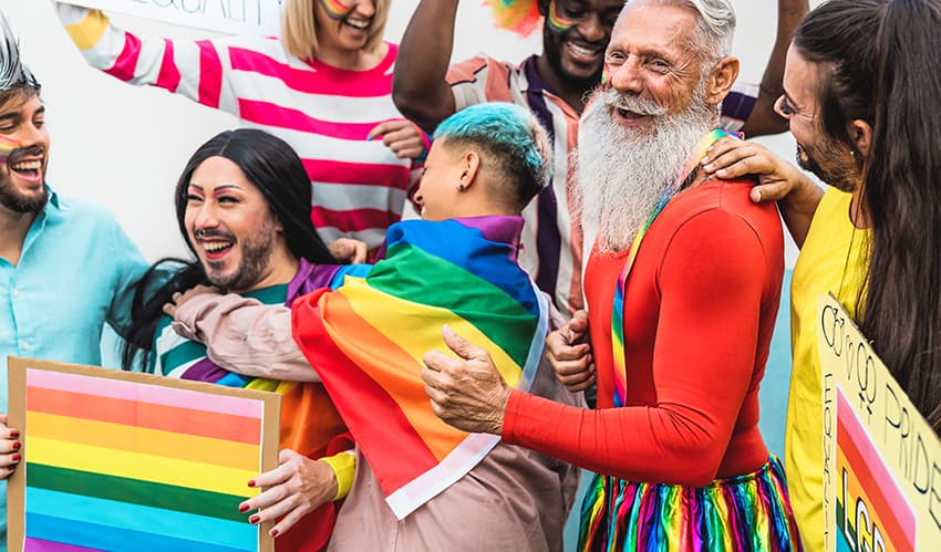 A group of people gather with rainbow flags and handmade signs, smiling