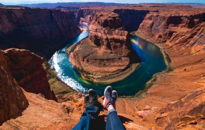 A couple dangle their feet on the edge of the Grand Canyon, the Colorado River visible below