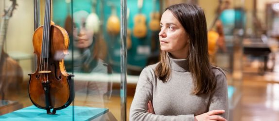 a woman stands next to a museum display of a violin